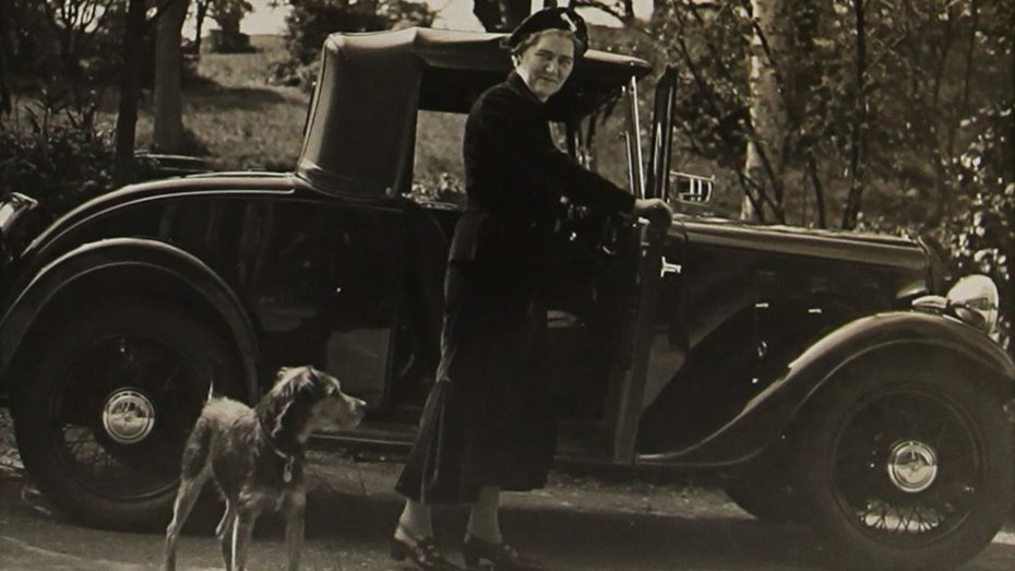 Elizabeth Casson and her dog Bran stand next to a car